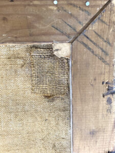 En gammel lap i hjørnet på bagsiden af det store maleri ved titlen Giv os i dag vort daglige brød af Cristian Aigens